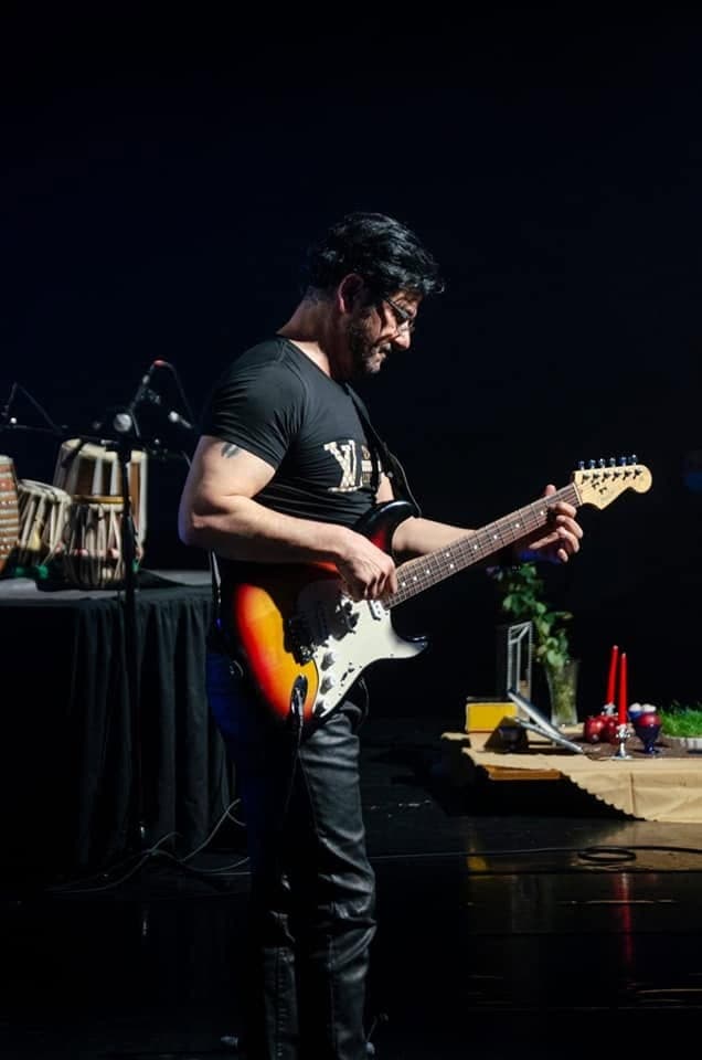 Taher Shubab playing an electric guitar on a dark stage
