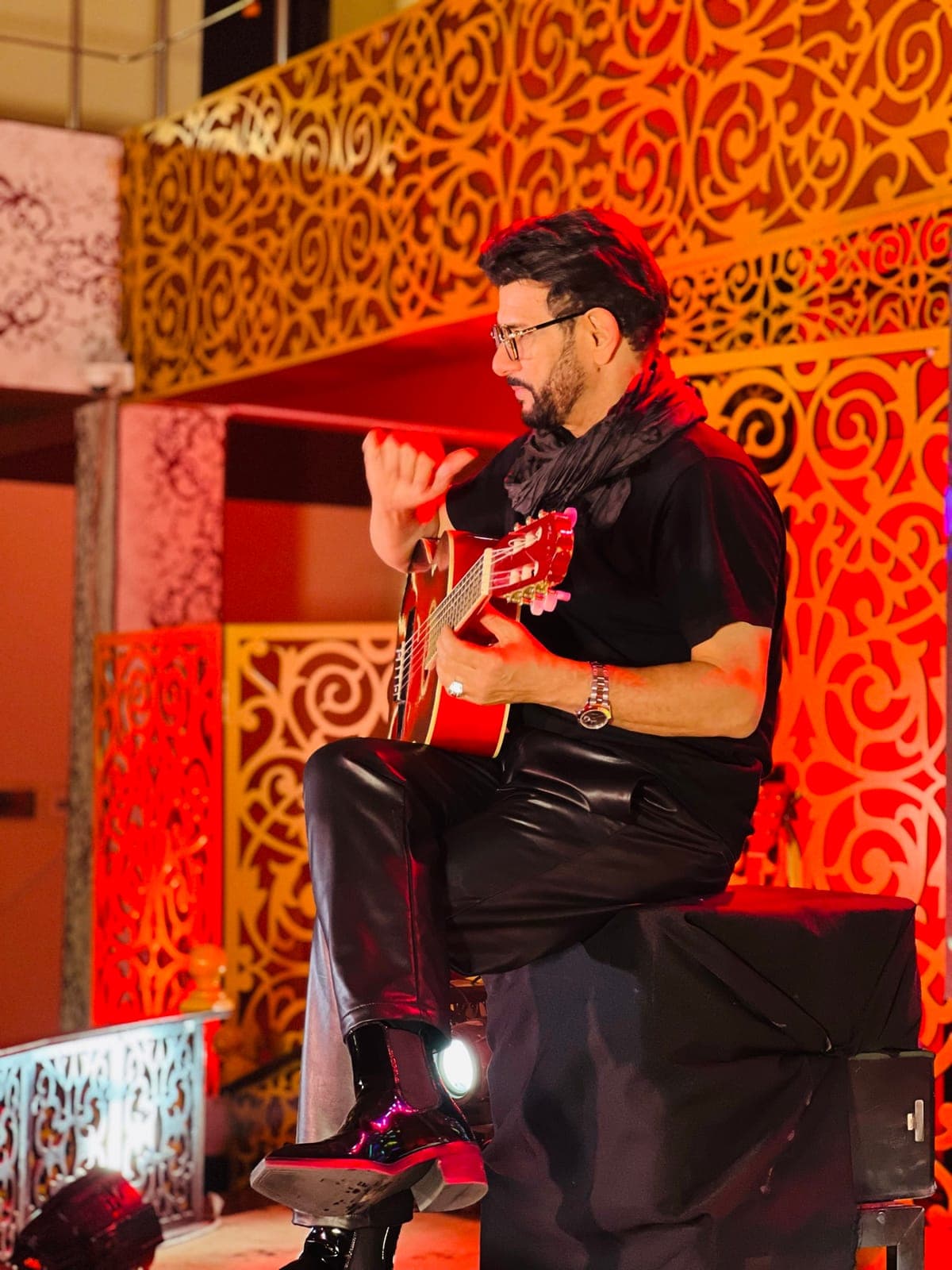 Taher Shubab playing acoustic guitar under amber stage light